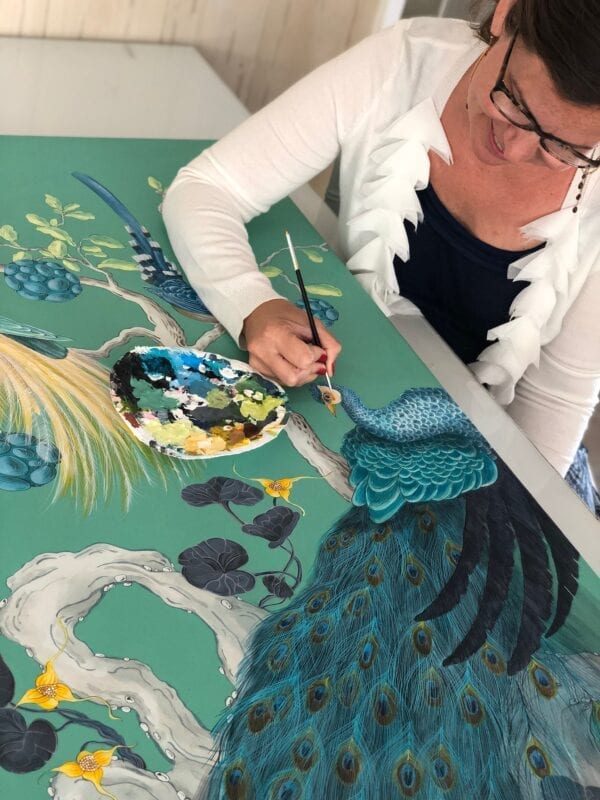 A woman painting a peacock on a table.