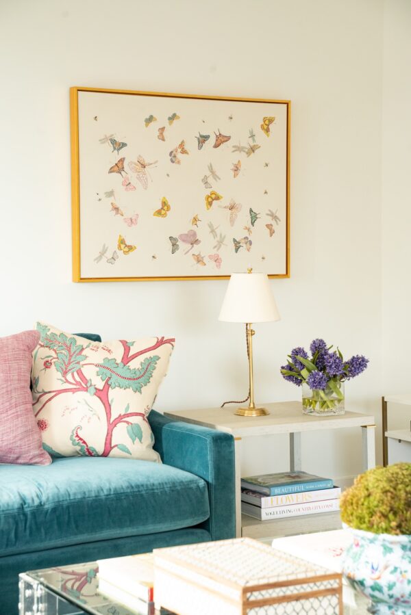 A living room with a teal "Daydream" Chinoiserie couch and butterfly print flowers on the wall.